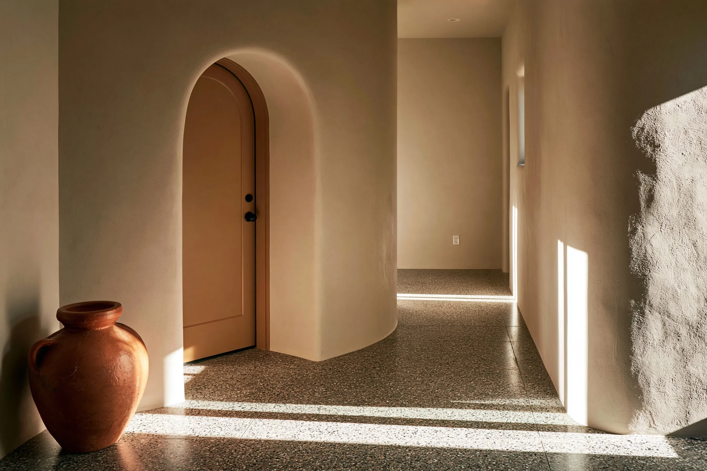Entry hall and corridor with a salt-and-pepper fine-aggregate polished concrete floor, an arched stucco doorway and a terracotta pot
