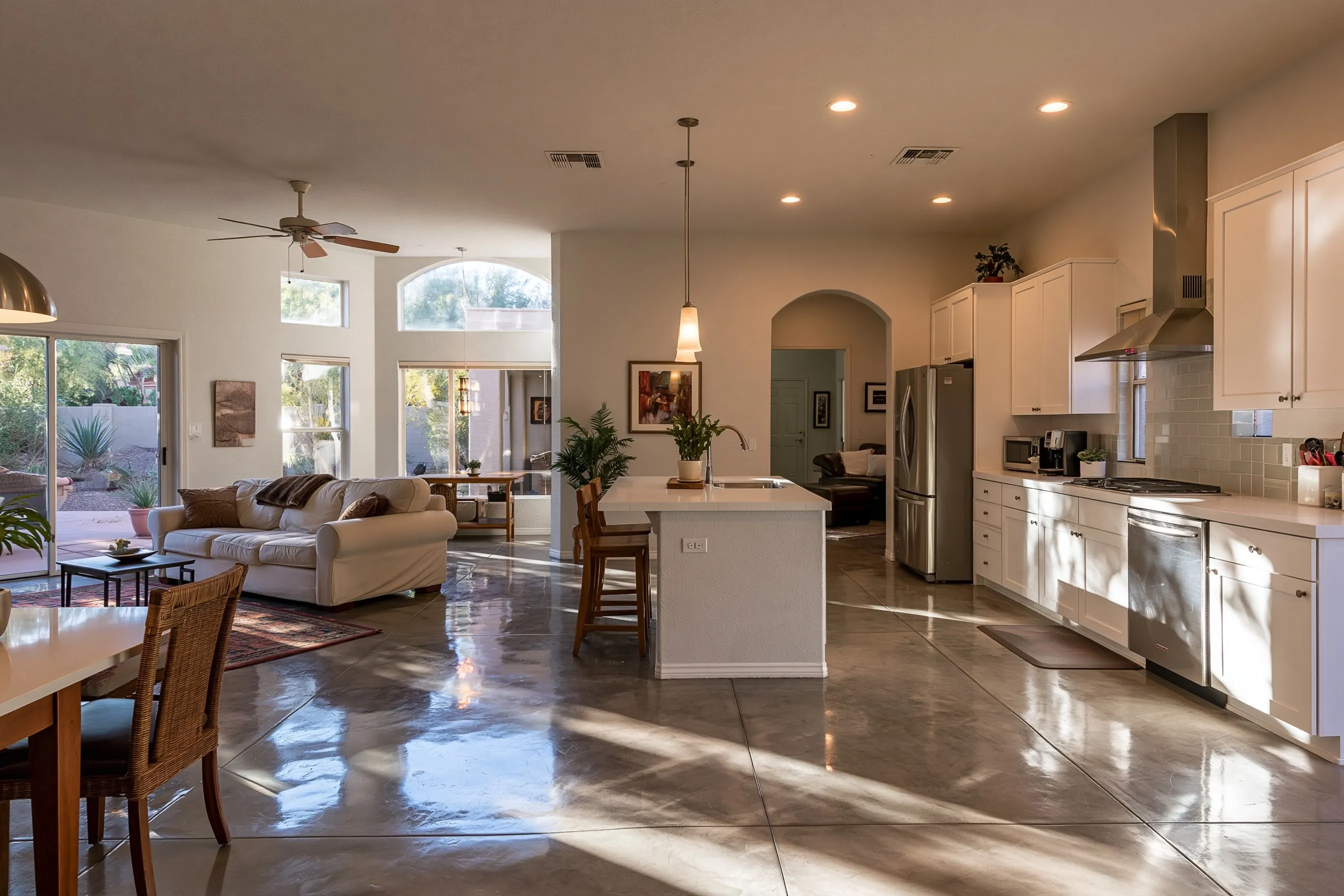Kitchen and great room of a newer Phoenix-valley house with a warm grey polished concrete floor, window light reflections, white shaker cabinets and stucco walls